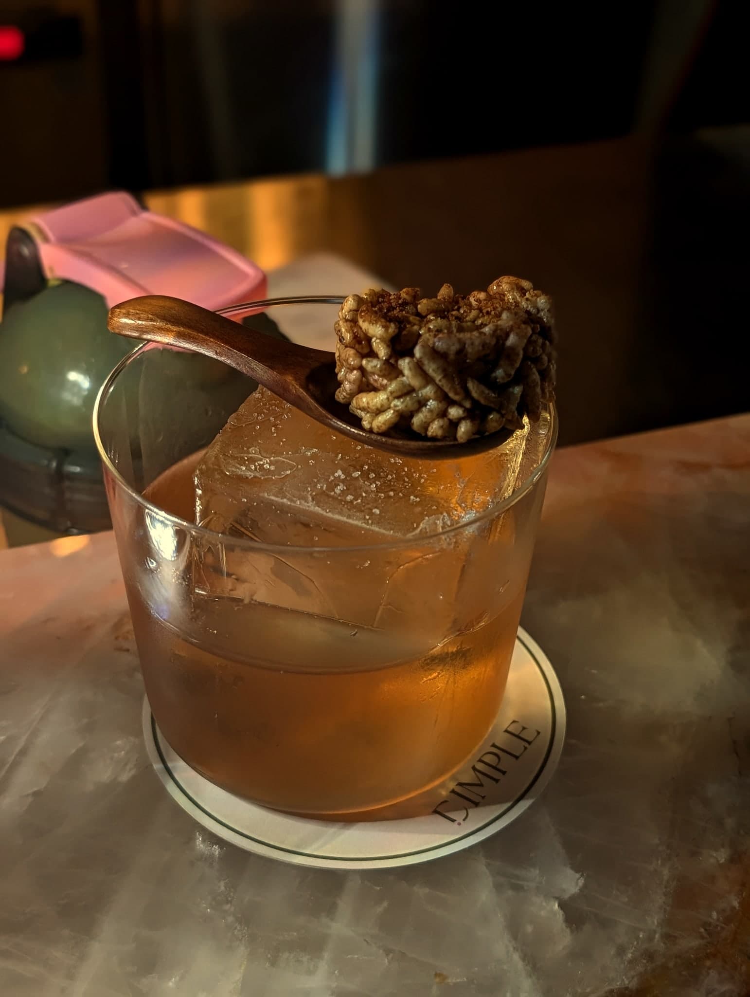 Shrimp & Sausage at Dimple — amber bourbon over a large rock with a puffed-rice cracker on a wooden spoon